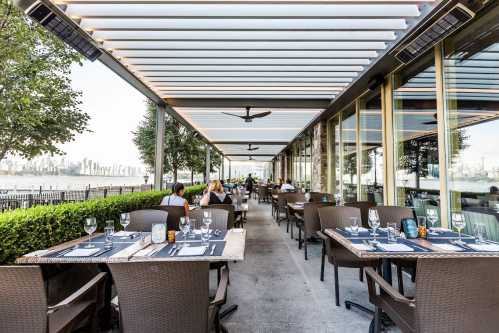 Outdoor dining area with tables set for guests, greenery, and a view of the skyline in the background.