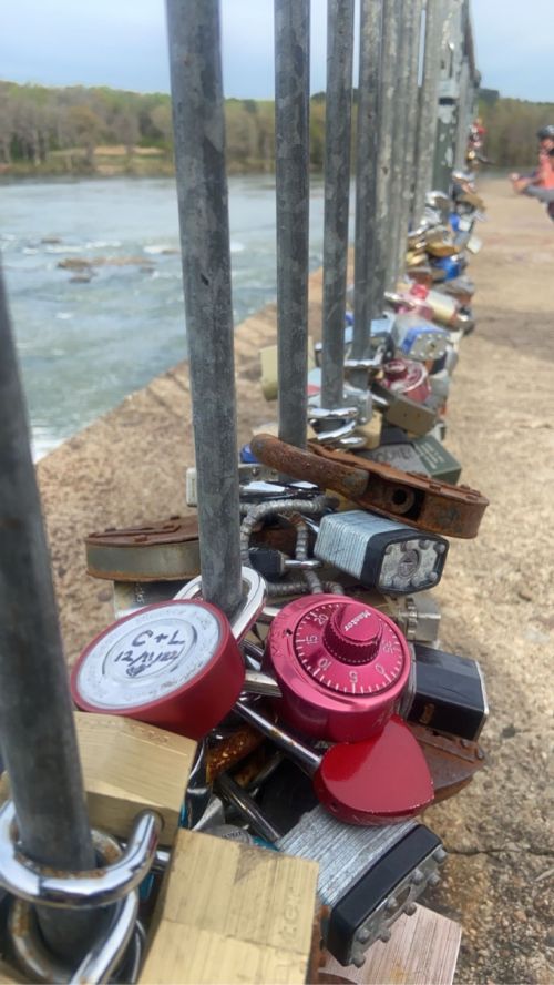A row of colorful padlocks attached to a railing by a river, symbolizing love and commitment.