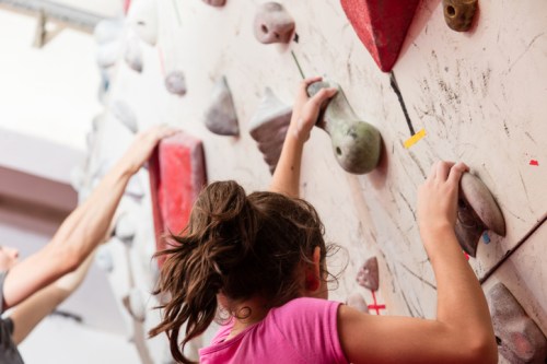 A child and an adult climbing on a bouldering wall, focusing on different holds.