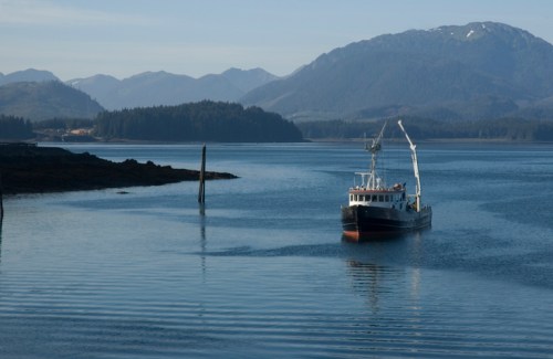 A fishing boat navigates calm waters with mountains in the background on a clear day.