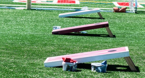 Three bean bag toss boards on green turf, with bags and containers nearby.