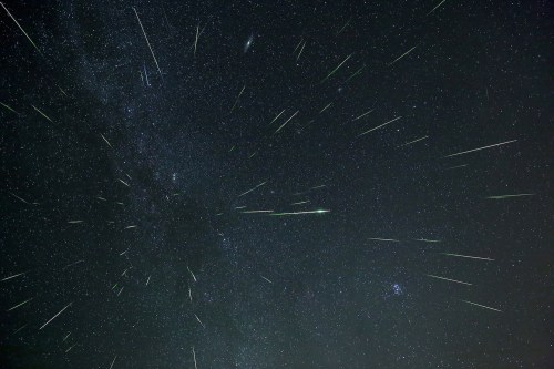 A starry night sky filled with numerous shooting stars and the Milky Way galaxy in the background.
