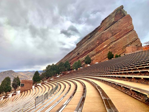 A view of the Red Rocks Amphitheatre, showcasing its iconic seating and surrounding rocky landscape under a cloudy sky.
