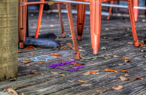 Colorful beads scattered on a wooden deck, with metal chairs and fallen leaves in the background.