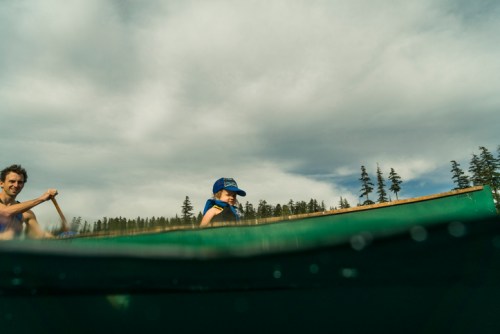 Two people in a canoe on a lake, with trees in the background and a cloudy sky above.