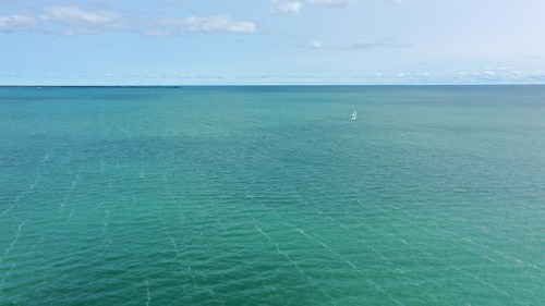 A serene view of calm turquoise waters with a small sailboat in the distance under a clear blue sky.