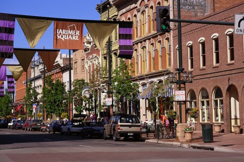A vibrant street scene in Larimer Square, featuring historic buildings, banners, and parked cars under a clear blue sky.