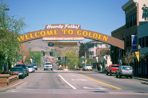 A welcoming arch over a street reads "Howdy Folks! Welcome to Golden," with shops and trees lining the road.