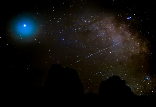 A starry night sky with a bright blue celestial object, a galaxy, and a shooting star above dark silhouettes of mountains.
