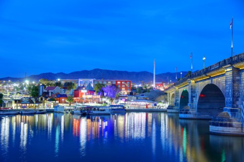 A scenic view of a bridge at dusk, reflecting lights on the water with mountains in the background.