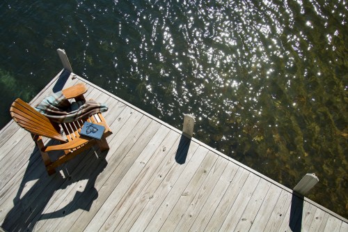 A wooden dock with an Adirondack chair and a blanket, overlooking shimmering water.