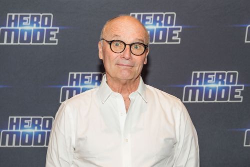 A bespectacled man in a white shirt poses in front of a "Hero Mode" backdrop.