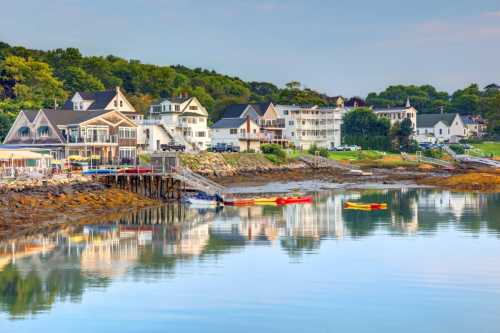 Coastal scene with colorful kayaks on calm water, surrounded by charming houses and lush greenery.