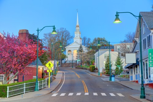 A quiet street scene at dusk, featuring a church steeple, blooming trees, and charming buildings.