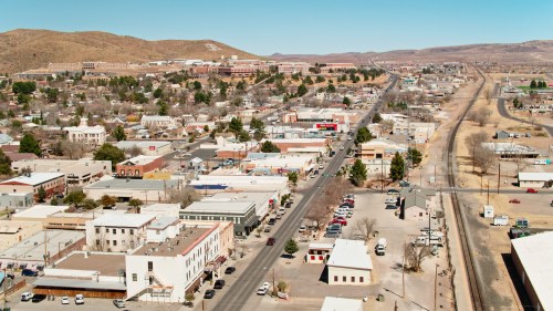 Aerial view of a small town with streets, buildings, and mountains in the background under a clear blue sky.