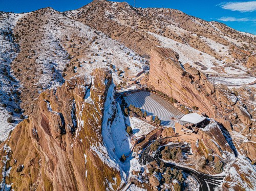 Aerial view of Red Rocks Amphitheatre surrounded by snow-covered mountains under a clear blue sky.