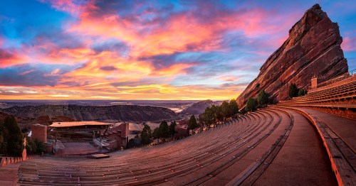 A panoramic view of Red Rocks Amphitheatre at sunset, showcasing vibrant skies and empty seating against rocky formations.