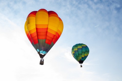 Two colorful hot air balloons float against a blue sky with wispy clouds.