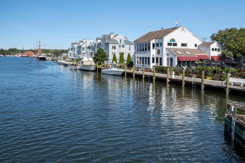 A serene waterfront scene with boats docked alongside charming houses under a clear blue sky.