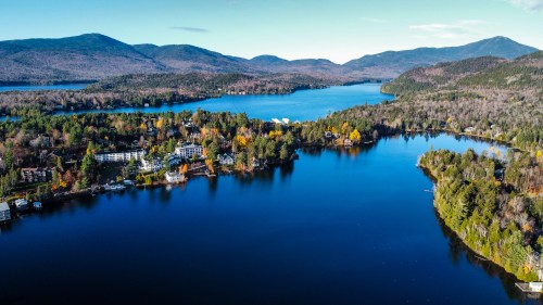 Aerial view of a serene lake surrounded by mountains and colorful autumn trees, with a small town along the shore.