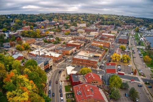 Aerial view of a vibrant town with colorful trees, buildings, and streets under a cloudy sky.