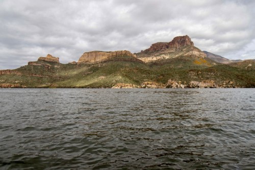 A serene lake with rippling water, surrounded by rugged mountains under a cloudy sky.