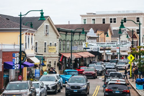 A busy street lined with shops and cars, featuring colorful buildings and street signs in a quaint town.