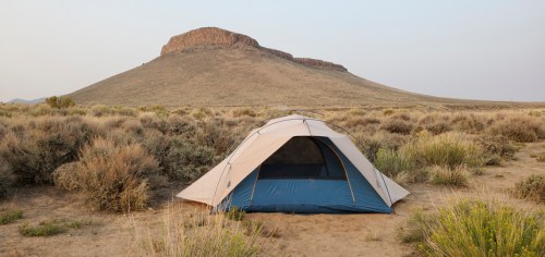 A tent set up in a dry, grassy landscape with a rocky hill in the background under a clear sky.
