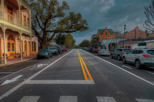 A quiet street lined with parked cars and historic buildings under a cloudy sky.