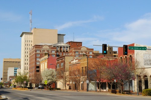 Downtown scene featuring a mix of historic and modern buildings, with traffic lights and blooming trees along the street.