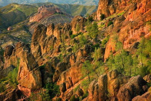 A scenic view of rugged rock formations and green trees on a mountainous landscape during golden hour.
