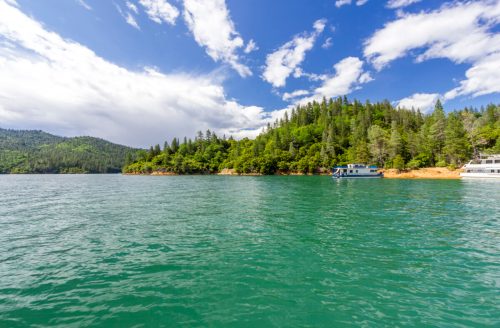 A serene lake surrounded by lush green hills and a partly cloudy sky, with boats docked along the shore.