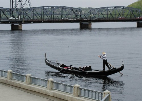 A gondola on a river with a person in striped attire rowing near a bridge in the background.