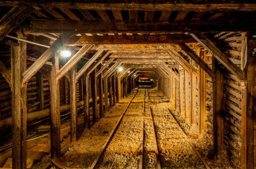 A dimly lit underground mine tunnel with wooden beams and tracks leading into the distance.