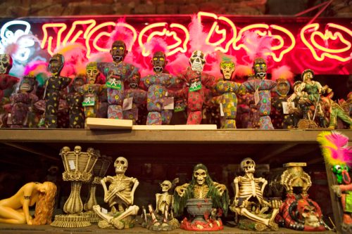 A colorful display of voodoo dolls and skeleton figurines under a neon sign, showcasing a vibrant, eclectic atmosphere.