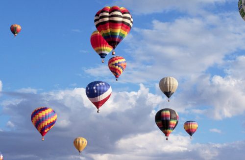 A colorful array of hot air balloons floating in a blue sky with fluffy clouds.