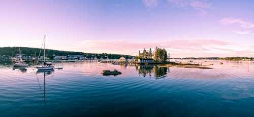 A serene harbor at sunset, featuring boats and a small island with trees, reflecting on calm waters.