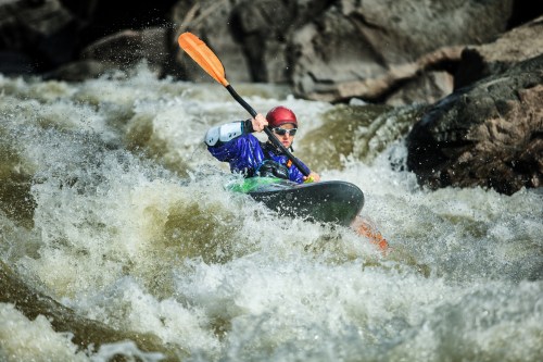 A kayaker navigates through turbulent whitewater rapids, wearing a helmet and paddling with determination.