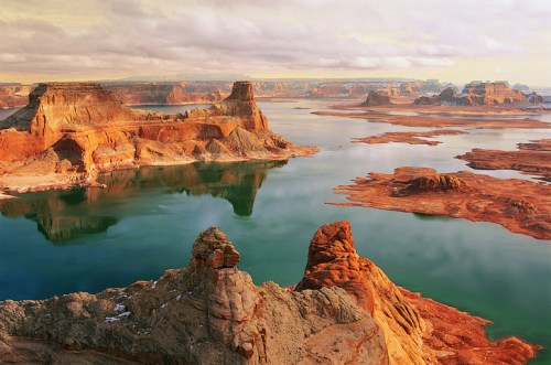 A serene landscape of red rock formations and calm waters under a cloudy sky, showcasing natural beauty and tranquility.