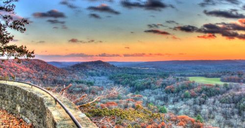 A scenic view of rolling hills at sunset, with vibrant autumn foliage and a colorful sky.