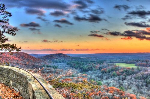 A scenic view of rolling hills and valleys at sunset, with vibrant colors in the sky and autumn foliage.