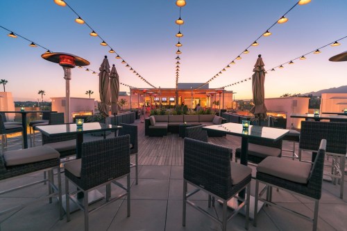 Rooftop lounge with string lights, seating areas, and a sunset view, creating a cozy atmosphere.