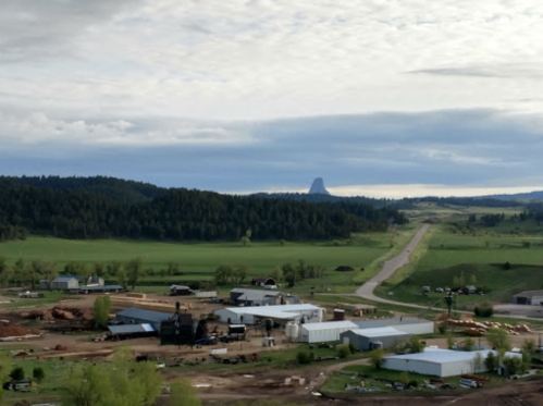 A rural landscape featuring a farm, scattered buildings, and a distant mountain under a cloudy sky.