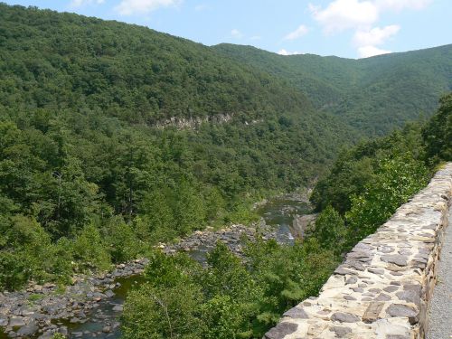 A scenic view of a river winding through lush green mountains under a blue sky with scattered clouds.