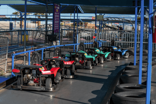 A row of colorful go-karts parked on a track under a blue canopy at an amusement park.