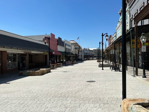 A wide, empty street lined with shops and cafes under a clear blue sky.