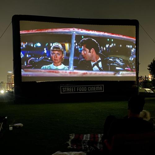 Outdoor movie screening at night featuring a scene from a classic film with two characters in a car.