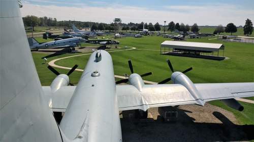 View from above an aircraft, showcasing a museum with various planes displayed on a grassy field.