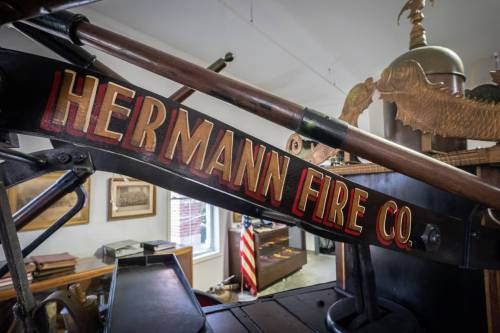 Close-up of a vintage fire truck's sign reading "Hermann Fire Co." in a museum setting.
