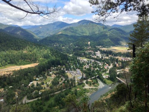 A scenic view of a valley with a small town, surrounded by lush green mountains and a winding river below.